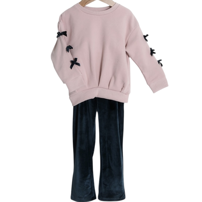 Girls blush pink sweatshirt with black bow sleeve details paired with dark velvet pants on hanger