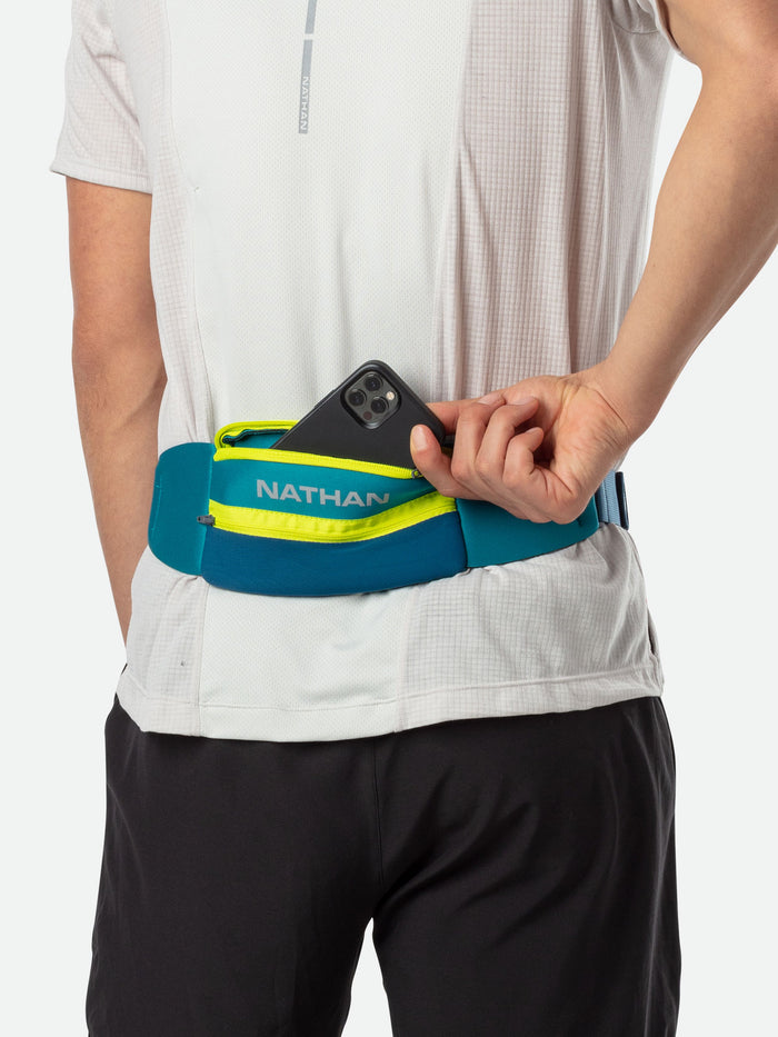 color:Storm Green/Finish Lime||seo:Nathan 5K Waist Running Belt - Storm Green/Finish Lime - On Model - Runner Pulling Out Cell Phone From Storage Pocket
