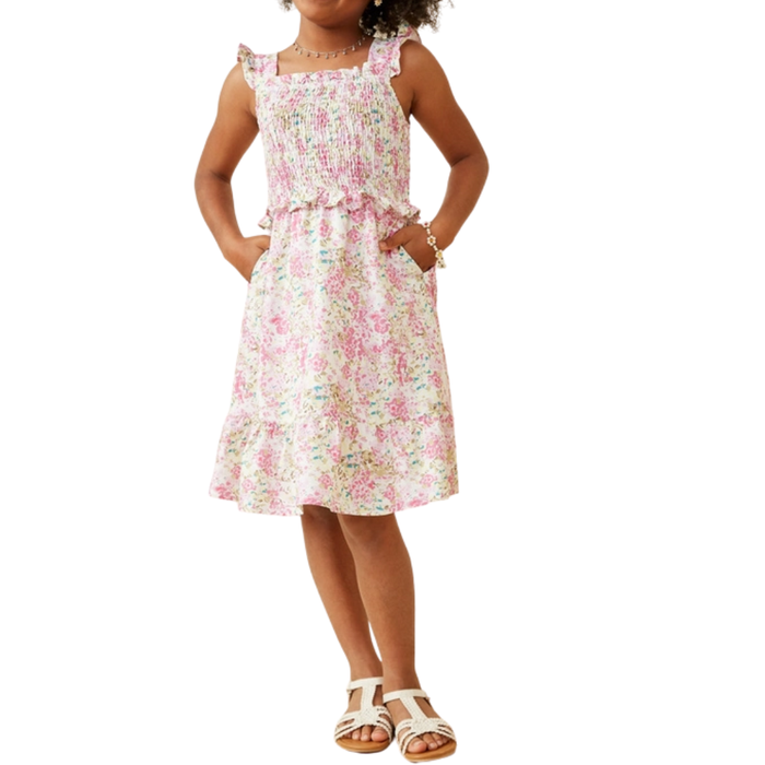Girl wearing a pastel floral smocked dress with ruffle straps and pockets, paired with white sandals.