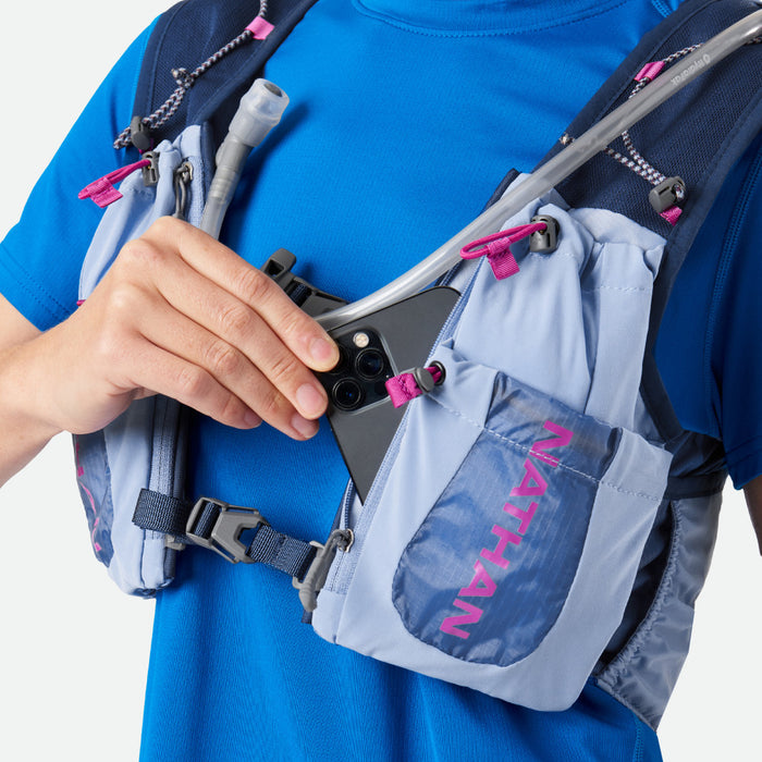 color:Periwinkle/Magenta||seo:Nathan VaporAiress 2.0 7 Liter Women's Hydration Pack - Periwinkle/Magenta - On Model - Model Pulling Cell Phone From Pocket